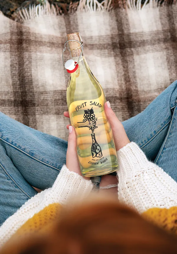 Person holding a bottle of E11even wine on a picnic blanket